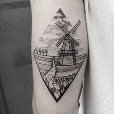 a black and white photo of a windmill tattoo on the right arm, with trees in the background