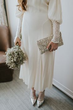 a pregnant woman in a white dress holding flowers and a clutch on her left hand