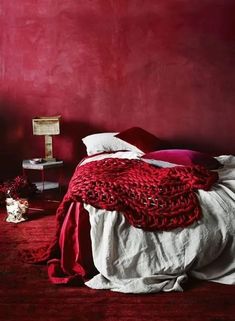 a bedroom with red walls and white linens on the bed, along with a crocheted blanket