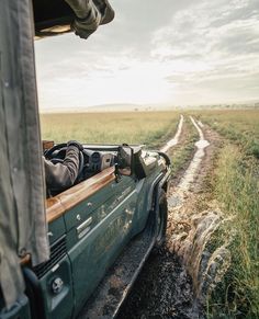 a man driving in the back of a pick up truck down a dirt road next to a field