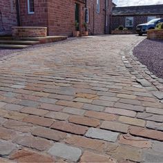 a cobblestone street with cars parked in the background