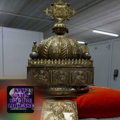 an ornately decorated golden clock on top of a red pillow in a room with white walls