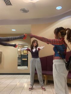 two girls are standing in the lobby with their arms spread out and one girl is wearing spider - man costume