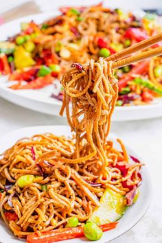 chopsticks lifting noodles from a plate with vegetables and sauce on it, ready to be eaten