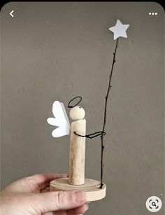 a hand holding a wooden stick with an angel on it and a star shaped tree branch