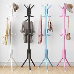 three coat racks with hats and sweaters hanging on them, next to a white wall