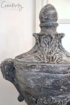 an ornate silver vase sitting on top of a wooden table next to a white wall