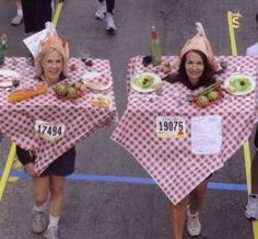 two women wearing hats and holding up picnic tables with food on them at an outdoor event