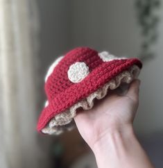 a hand holding a crocheted red and white hat