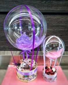 two clear vases with purple ribbons and decorations in them on a pink tablecloth