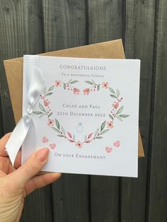 a person holding up a wedding card with a ring on the front and side, in front of a wooden fence