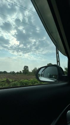 a car's side view mirror is shown in front of a field and power lines