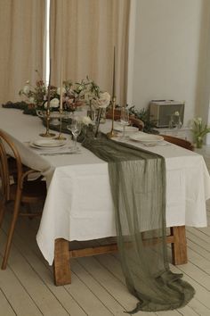 the table is set with white linens and flowers on it, along with two candles