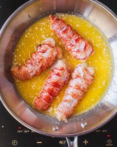 cooked lobsters are being prepared in a pan on the stove top with yellow liquid