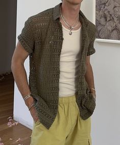 a man standing in front of a white wall wearing yellow shorts and a green cardigan