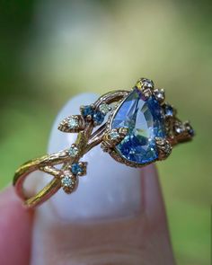 a close up of a person's hand holding a ring with a blue stone