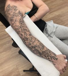 a woman sitting on the floor with her arm covered in flowers and leaves, holding a towel