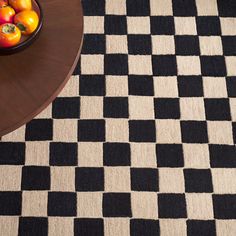 a black and white checkered rug next to a bowl of fruit on a table