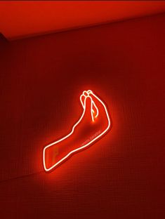 a red neon sign that is on the floor in front of a wall with a hand