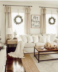 a living room filled with white furniture and christmas wreaths on the window sill