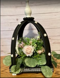 a vase filled with flowers and greenery on top of a wooden table next to a wall