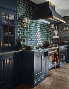 a kitchen with dark blue cabinets and green tile backsplash, an oven hood over the stove