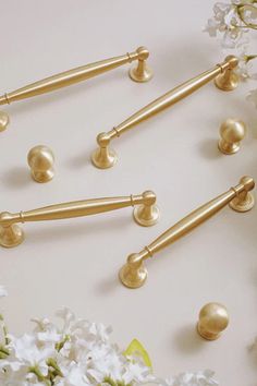 several gold handles and knobs on a white surface with flowers in the foreground