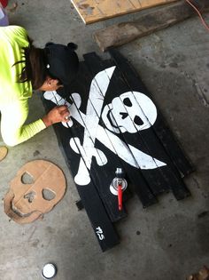 a woman is painting a pirate sign with white paint on the ground next to a skull and crossbones