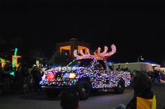 a truck decorated with christmas lights driving down the street in front of a crowd at night