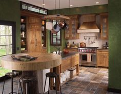 a kitchen with green walls and wooden cabinetry, counter tops, pots and pans hanging from the ceiling