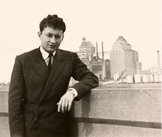 a man in a suit leaning against a wall with his hands on his hips and looking at the camera