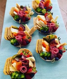 fruit and crackers are arranged in bowls on a blue tablecloth with silverware