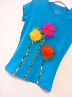 a blue t - shirt with three colorful feathers on it and two straws sticking out of the back