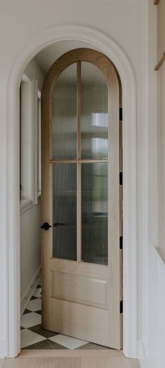 an arched wooden door with glass panels in a white house entryway that leads to a checkered tile floor