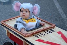 a baby in a mouse costume sitting on top of a wooden cart with metal bars