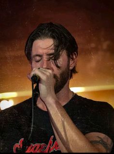 a man with long hair and beard holding a microphone to his face while standing in front of a stage