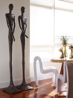 two metal statues sitting on top of a wooden floor next to a table and chairs