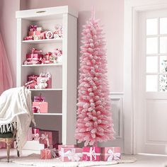 a pink christmas tree with presents under it in a living room next to a book shelf