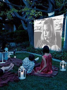 two people sitting on the grass watching a movie in front of a screen with candles