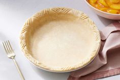 an uncooked pie crust next to a bowl of peaches and a fork