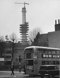 a double decker bus driving down a street next to tall buildings with cranes in the background