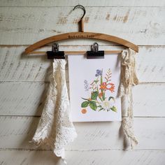 an art piece hangs on a wooden hanger with two laces hanging from it