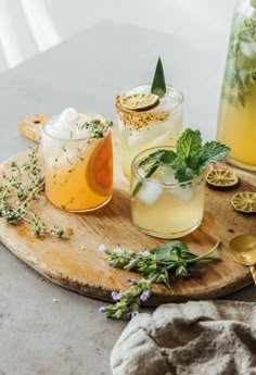 three glasses filled with different types of drinks on top of a wooden tray next to spoons