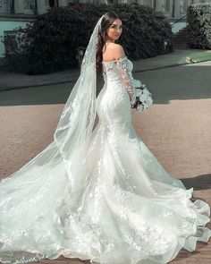 a woman in a wedding dress is standing on the sidewalk with her veil blowing in the wind