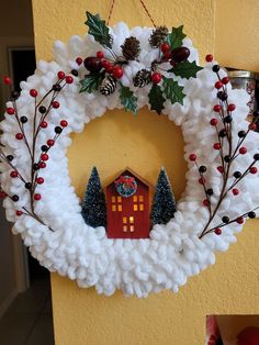 a christmas wreath hanging from the side of a yellow wall next to a red house