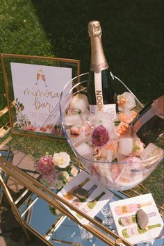 a table topped with a glass bowl filled with ice and flowers next to a bottle of champagne