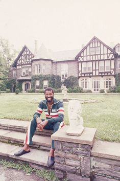 a man sitting on a stone bench in front of a large house