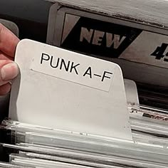 a person is holding up a label that says punk a - af in front of stacks of records