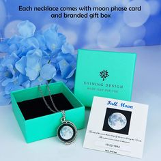 a blue box with a necklace in it sitting next to a white and blue flower