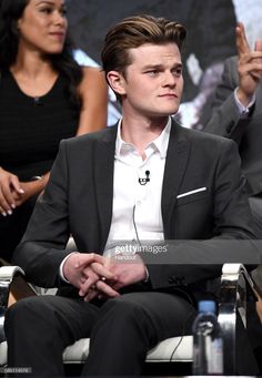 the actor is sitting in a chair with his hands up and two other people behind him